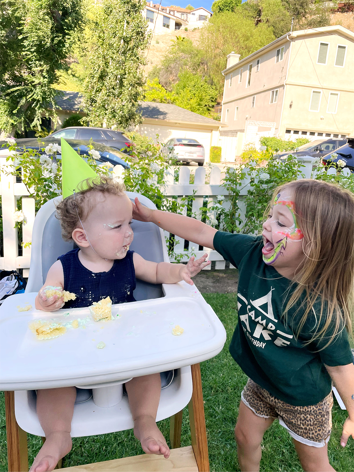 Child eating cake while his sister plays with him.