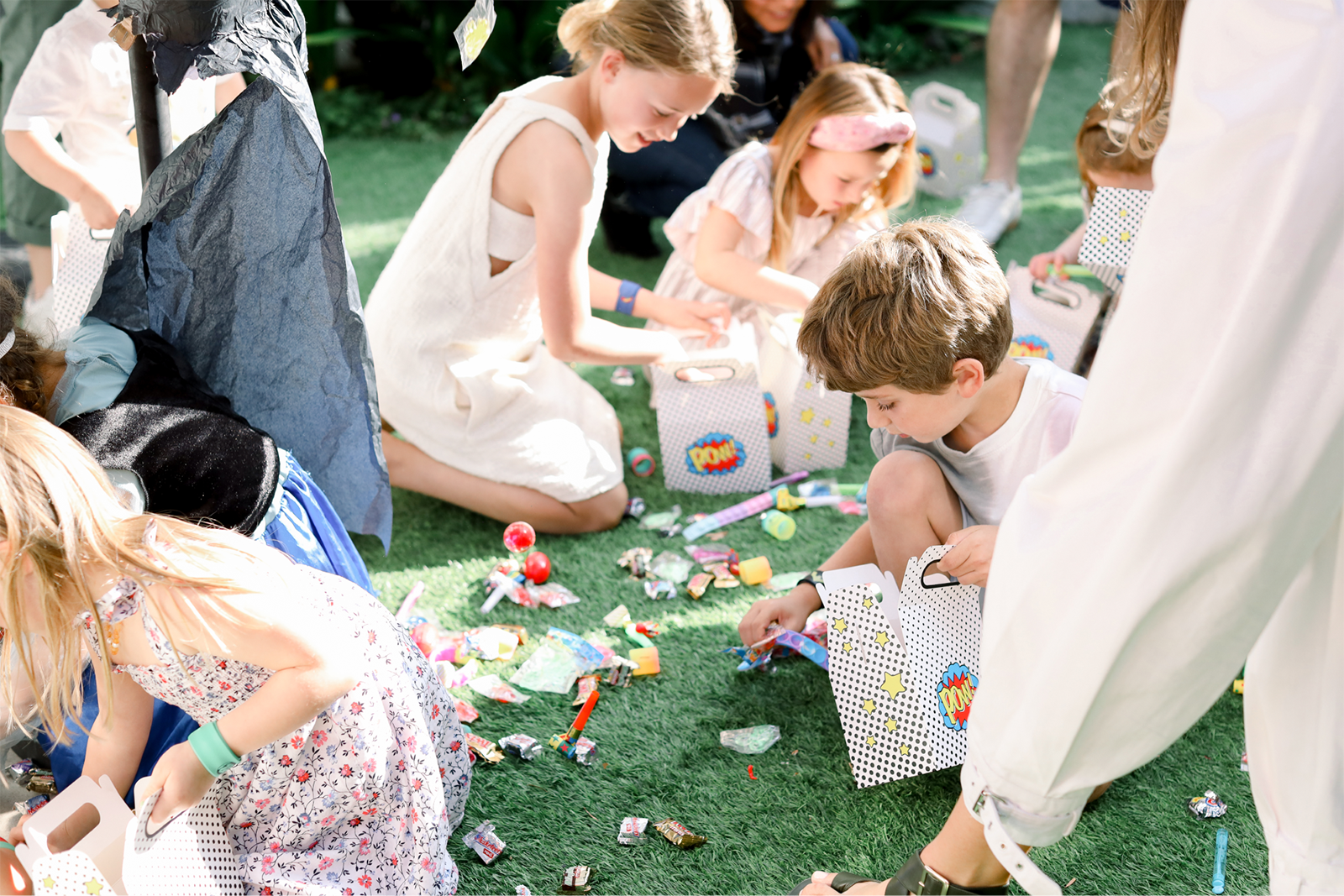 Kids on the ground gathering candy from the piñata and putting the candy in their bags.