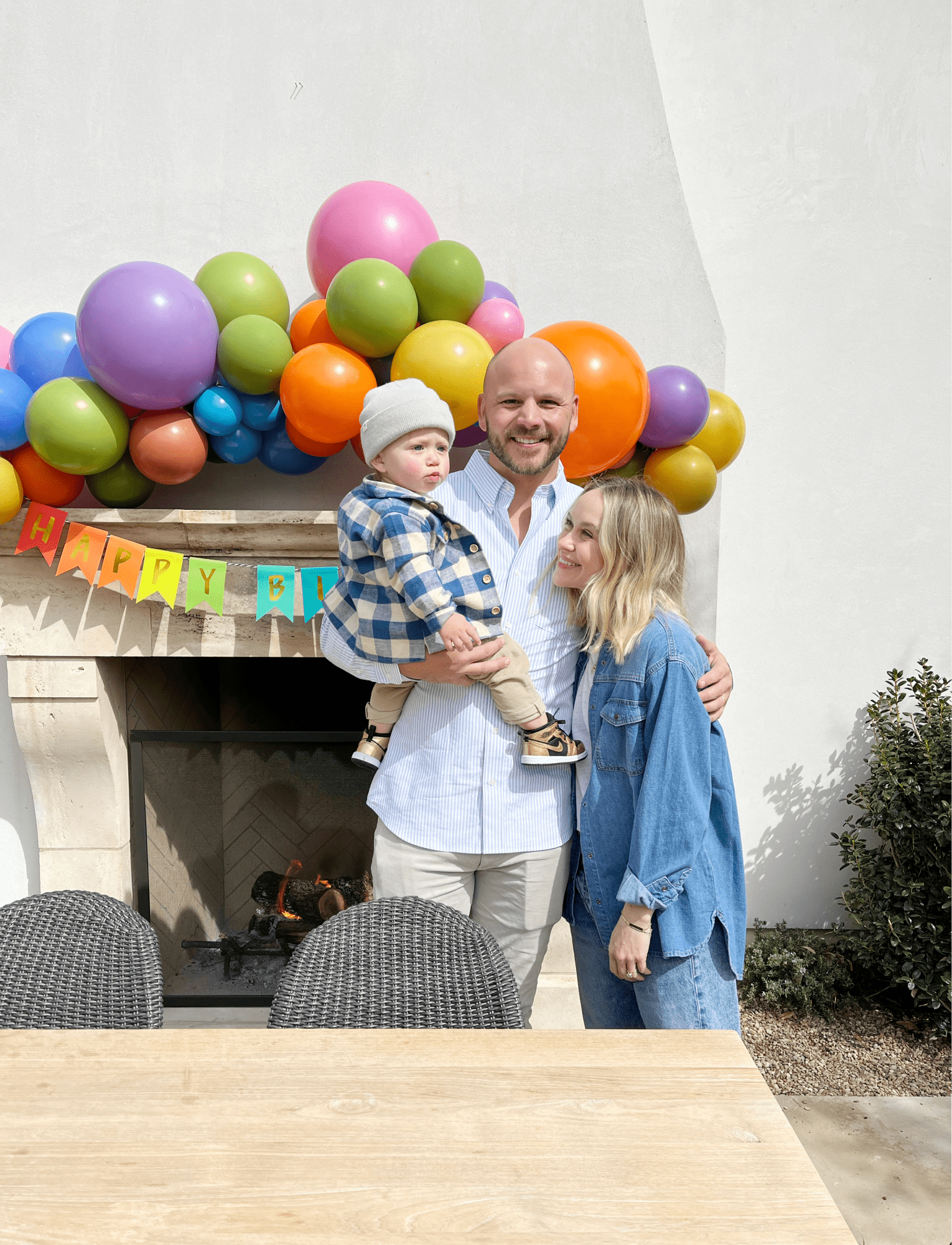 A family poses in front of a colorful balloon arch.