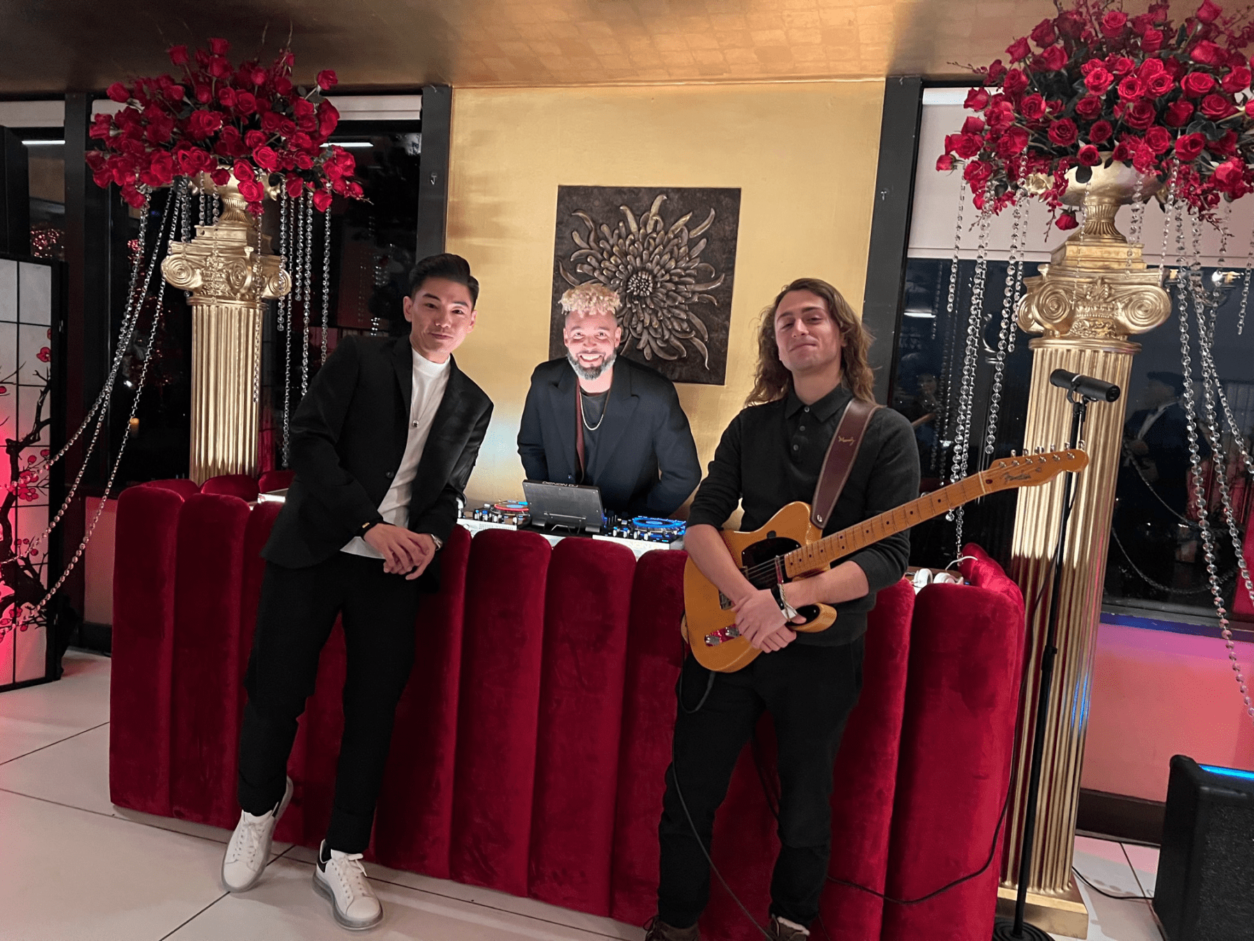 The DJ, the guitarist and a third man posing in front of the DJ booth.