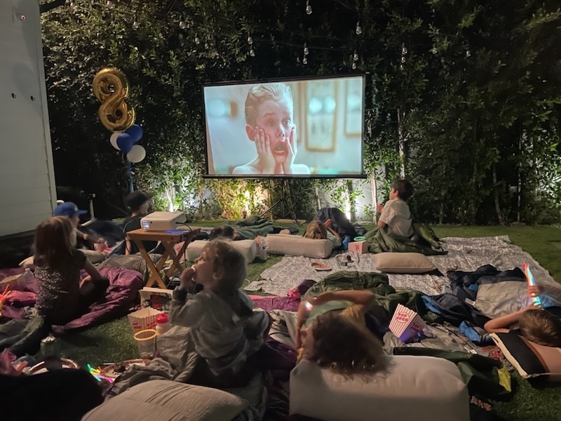 Kids watching Home Alone in a backyard while drinking out of glow in the dark cups.