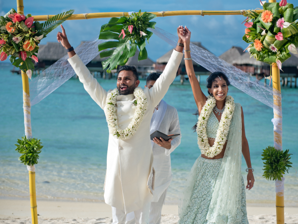 Priya and Sumanth smiling in front of the alter with their hands raised.s
