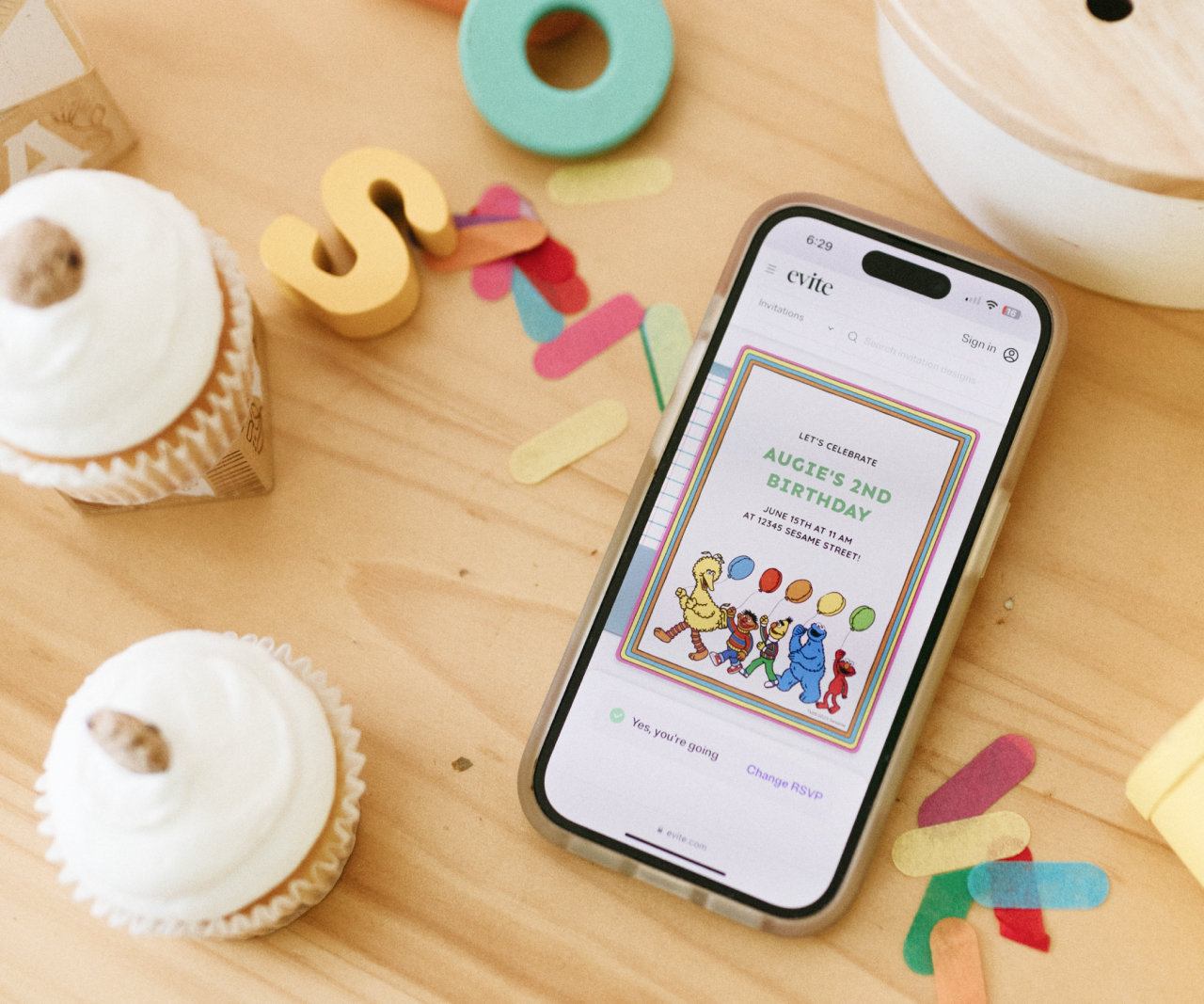 Phone with Sesame Street invitation on it surrounded by cupcakes.