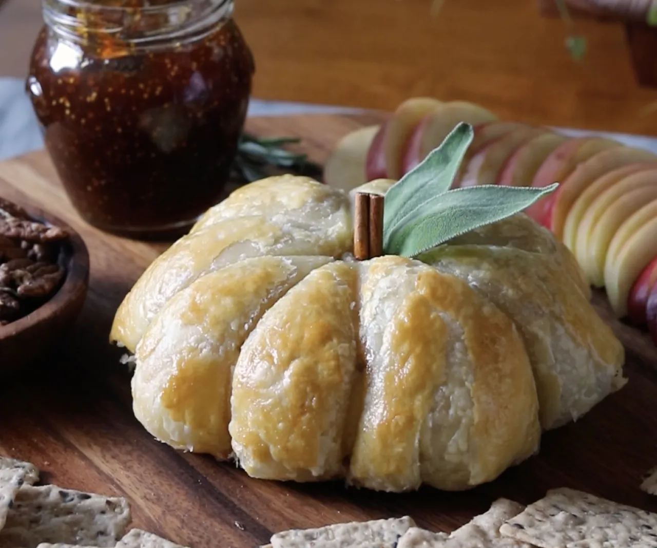 Baked puff pastry shaped like a pumpkin with cinnamon stick and sage leaf on wooden board.