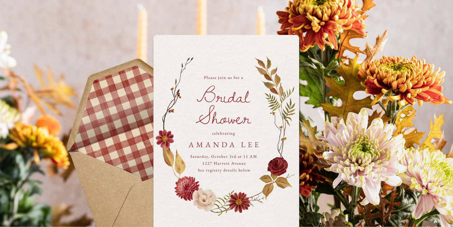 A cream Invitation with a garland of red flowers and green foliage. 
