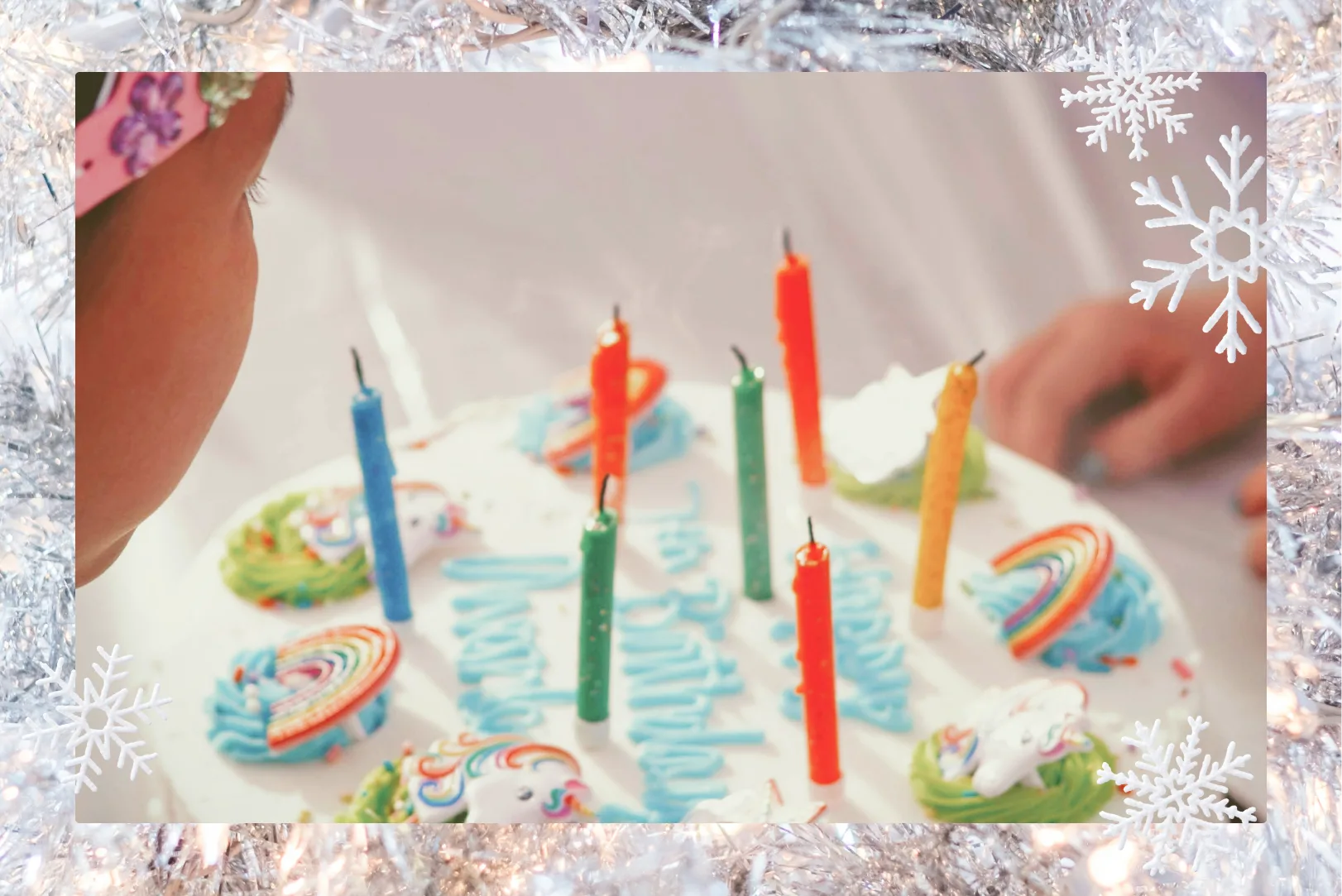 A birthday cake with colorful candles and a white snowflake border. 