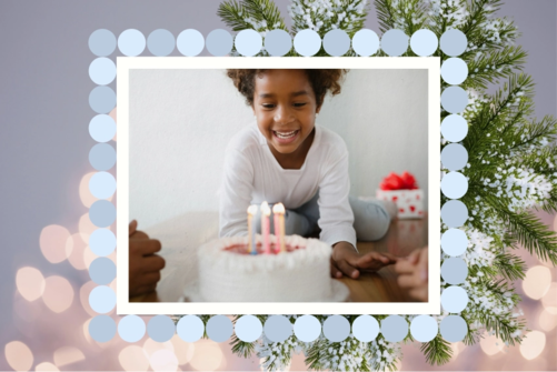 Child smiling at a birthday cake with lit candles, framed by a winter border with snowy pine branches and a ring of pale blue circles.