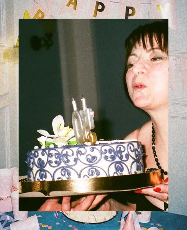 A woman blowing out candles on a decorated blue and gold cake.