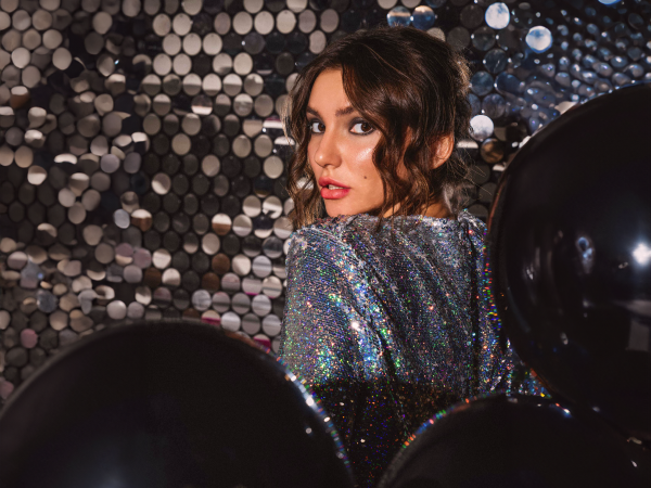 Woman in a sequin dress in front of a sequin backdrop and balloons.
