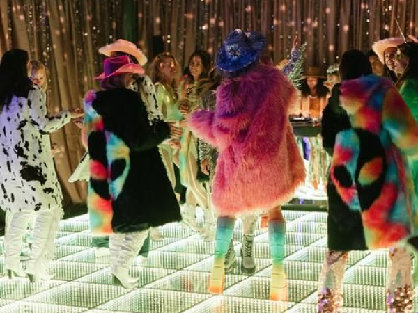 People dancing on a light-up dance floor while wearing cowboy hats and fuzzy coats.
