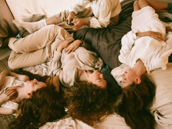 A group of women lying down on a pile of blankets and pillows.