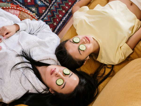 Two women lying down with cucumber slices over their eyes.