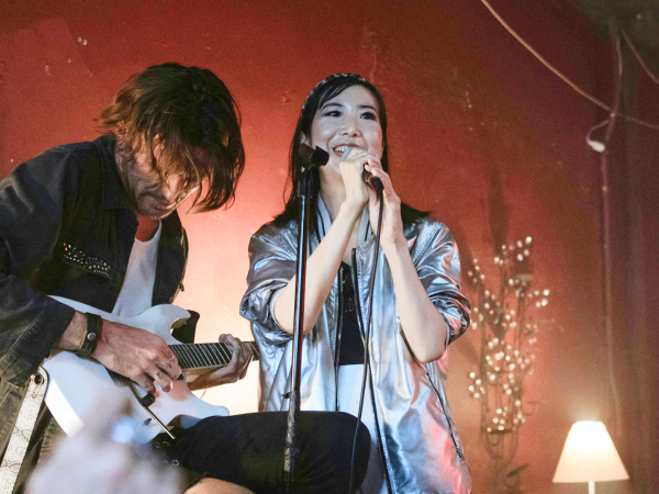 A woman singing into a microphone while a man plays guitar.