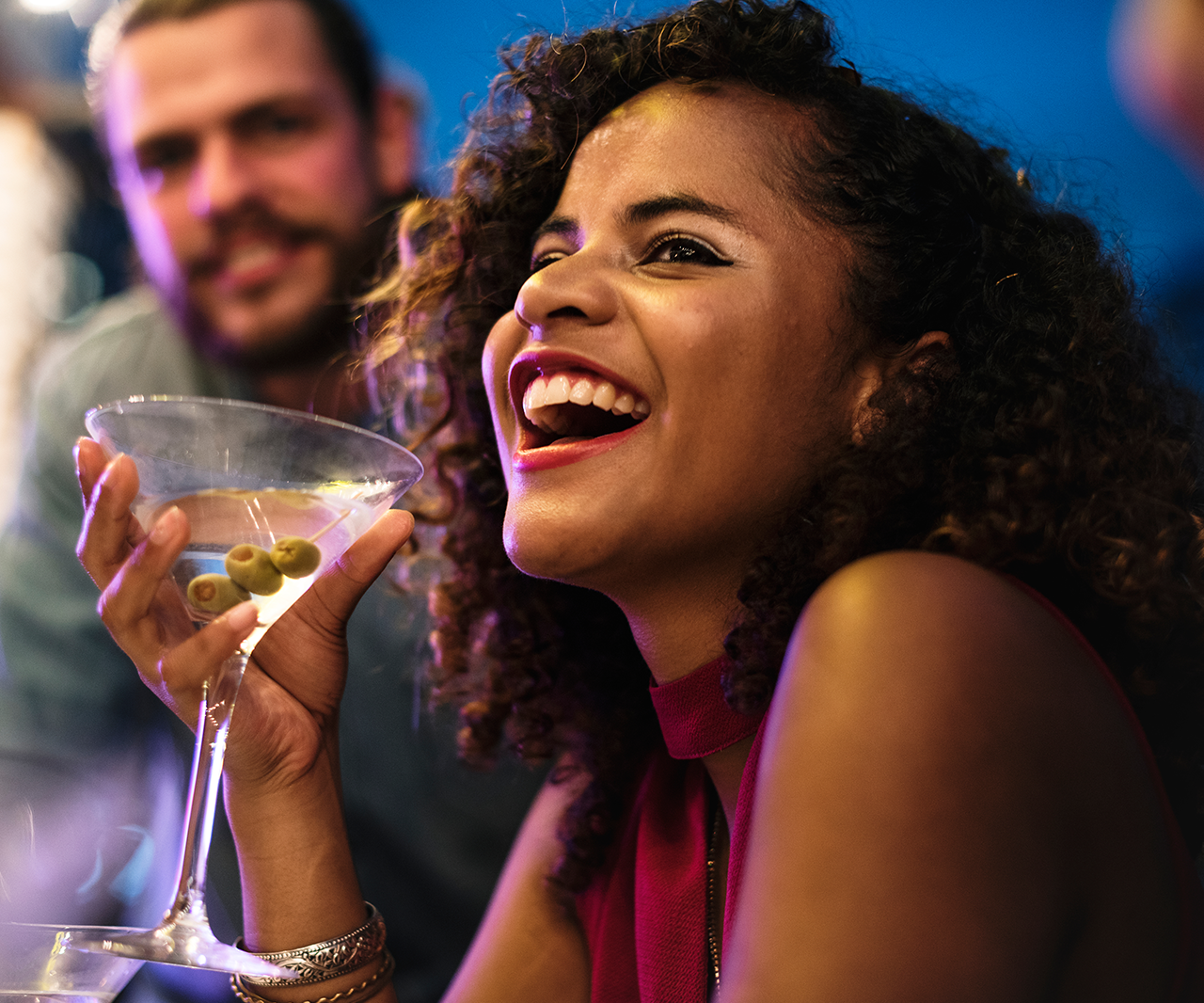 A woman laughing at a party while holding a martini.