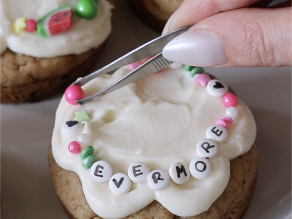 Close up of sprinkles being added onto a frosted chocolate chip cookie.