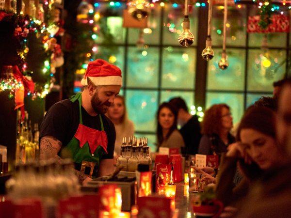 Bartender wearing a Santa hat and elf ears working at a festive bar.