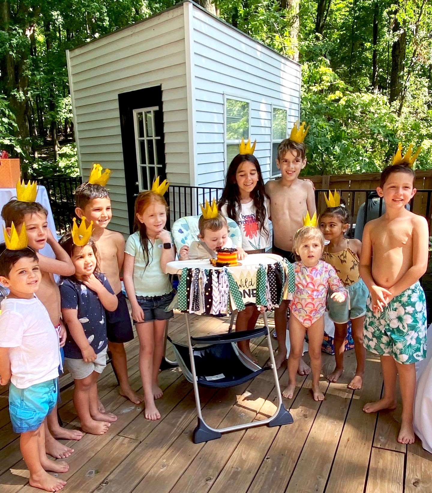 Kids at a birthday party wearing crowns while a child eats cake in the middle.