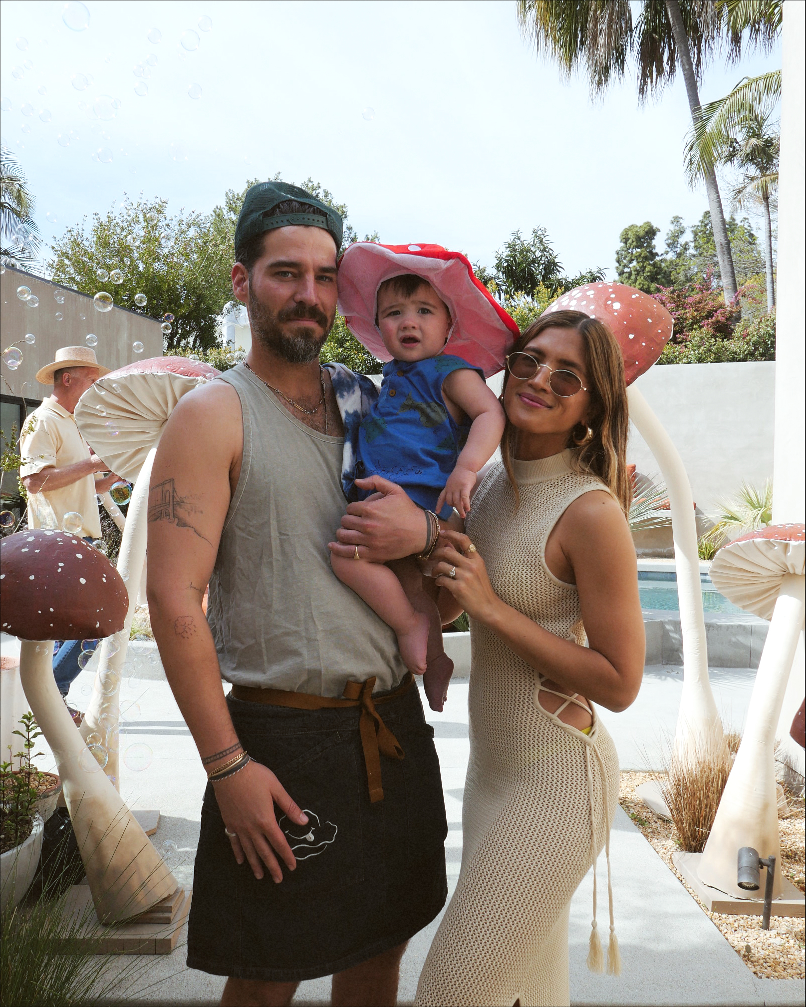 Parents pose with their baby who is wearing a mushroom hat.