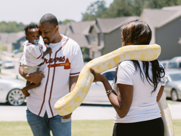 A woman holding a snake. A man holds a baby next to her.