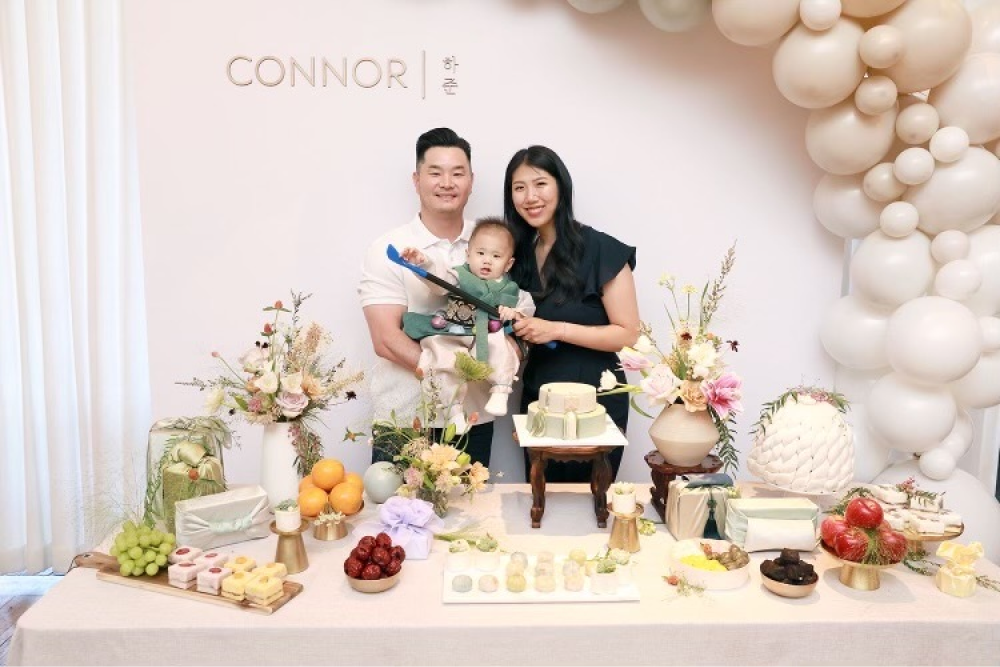 Connor and his parents in front of the accent wall and balloons.