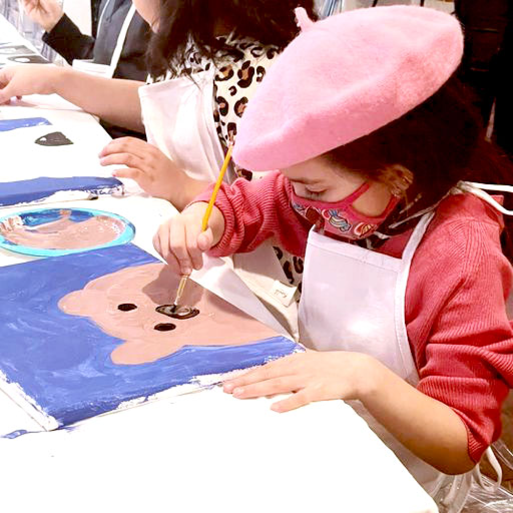 A little girl painting a bear on a canvas.