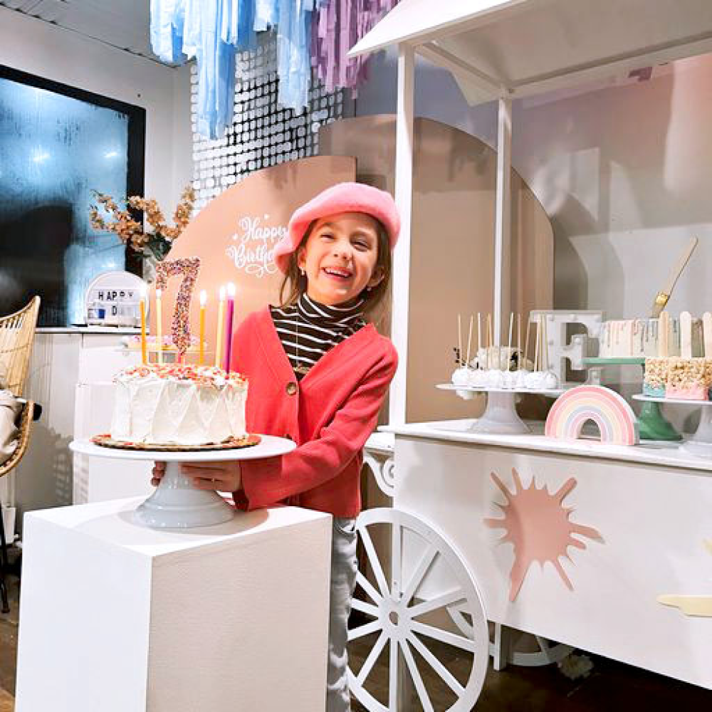 A little girl holding her birthday cake with the candles lit. She is smiling.