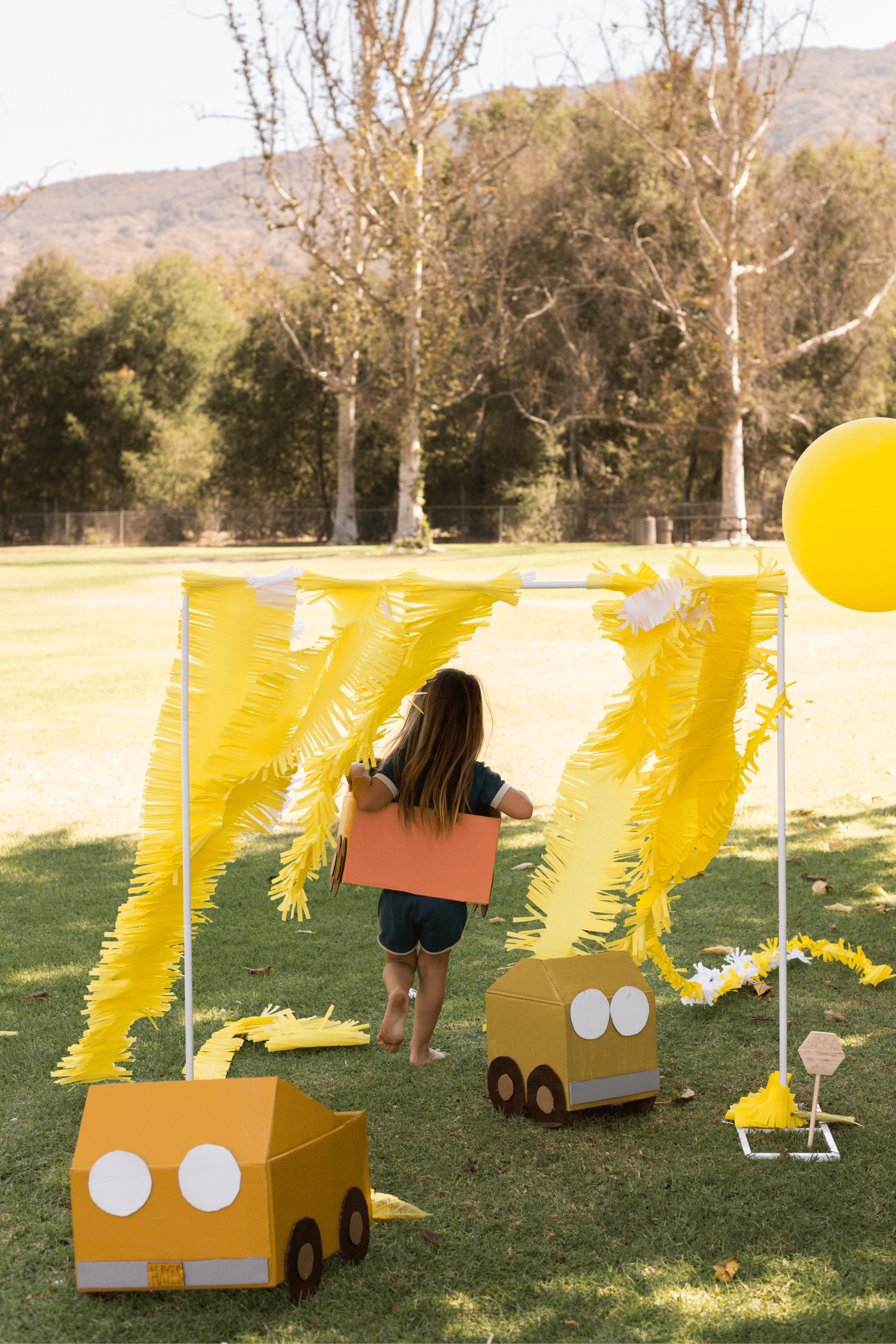 A kid in a cardboard car running through streamers.
