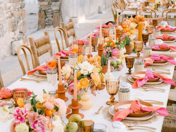 A colorful, summery outdoor dinner table with lots of flowers and candles.